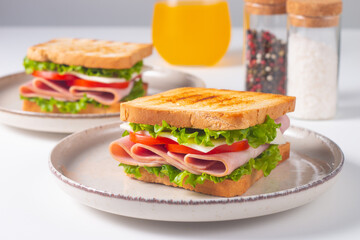 Close-up of two sandwiches with bacon, salami, prosciutto and fresh vegetables on rustic wooden cutting board. Club sandwich concept