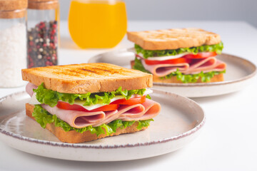Close-up of two sandwiches with bacon, salami, prosciutto and fresh vegetables on rustic wooden cutting board. Club sandwich concept