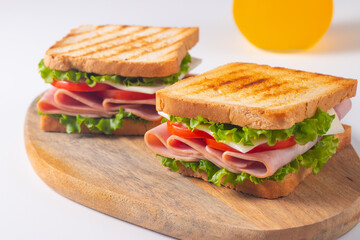 Close-up of two sandwiches with bacon, salami, prosciutto and fresh vegetables on rustic wooden cutting board. Club sandwich concept