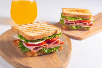 Close-up of two sandwiches with bacon, salami, prosciutto and fresh vegetables on rustic wooden cutting board. Club sandwich concept