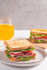 Close-up of two sandwiches with bacon, salami, prosciutto and fresh vegetables on rustic wooden cutting board. Club sandwich concept
