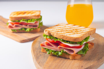 Close-up of two sandwiches with bacon, salami, prosciutto and fresh vegetables on rustic wooden cutting board. Club sandwich concept