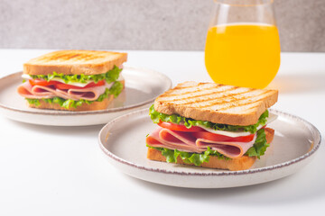 Close-up of two sandwiches with bacon, salami, prosciutto and fresh vegetables on rustic wooden cutting board. Club sandwich concept
