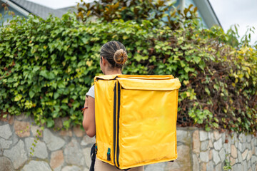 Hispanic food delivery girl with backpack, seen from behind, walking to complete her delivery job