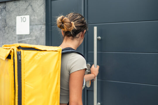 hispanic food delivery girl with yellow backpack pushing door to deliver order