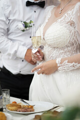 The bride is holding a glass of champagne while standing near the festive table.