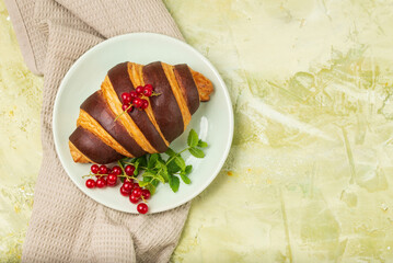 Chocolate croissant with red currants and fresh mint in green plate on  light green textured background top view with copy space