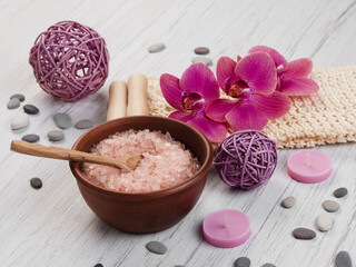 Spa bath salts in bowl with loofah, orchids and candle on wooden table