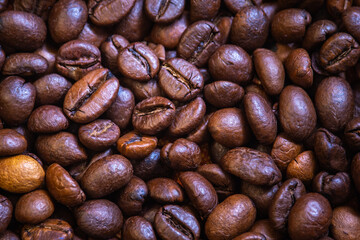 Coffee beans background photo taken in close up. Dark roasted brown beans with unique textures kept in pile. 
