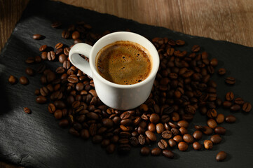 A composition with a cup of coffee and coffee beans scattered on the table