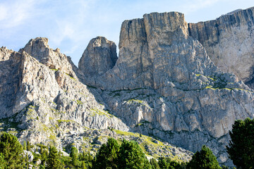 Majestic mountain cliffs tower over lush greenery in a serene landscape under bright blue skies