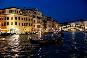 Gondola gliding through the illuminated canals of Venice at night beneath the historic Rialto Bridge