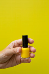 Woman's hand with yellow nails holding a bottle of yellow nail polish.