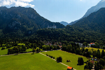 Majestic Neuschwanstein Castle nestled in the Bavarian Alps surrounded by lush greenery and distant mountains on a sunny day