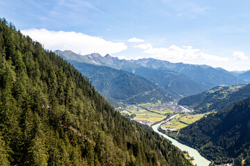 A breathtaking view of the green valley and river winding through mountains near a quaint village on a sunny day
