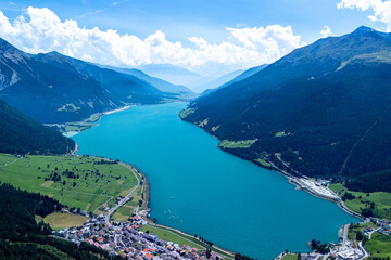 Stunning aerial view of a turquoise lake surrounded by mountains and green fields in the Swiss Alps on a clear summer day