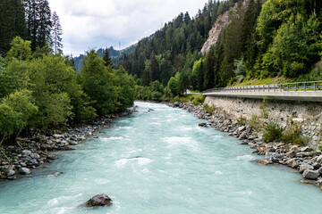 A serene river flows through a lush green valley in the mountains on a cloudy day, inviting quiet contemplation and nature exploration