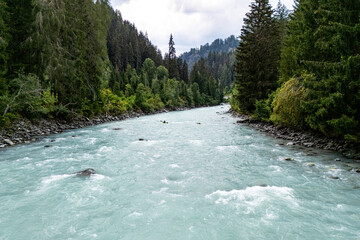 Tranquil mountain river flowing through lush green forest in a serene valley during a cloudy day