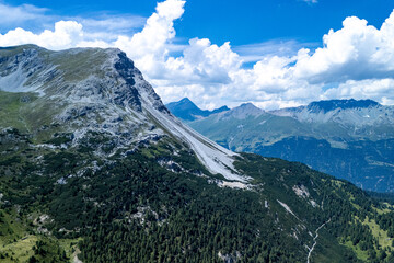 Majestic mountain landscape under a bright blue sky with fluffy clouds and lush green forests surrounding dramatic rock formations