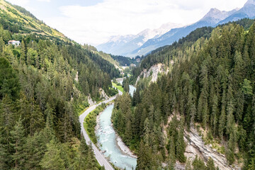 Aerial view of a winding river surrounded by dense forests and mountains during a clear day in a serene valley