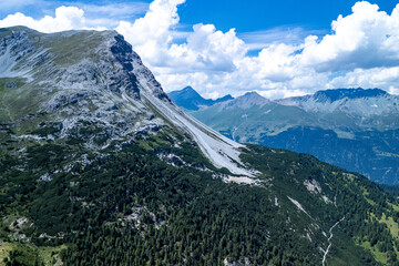 Stunning aerial view of rugged mountain landscape with lush forests under a dramatic sky in the Alps during midday