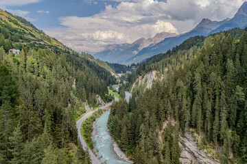 Aerial view of a winding river surrounded by lush green forests and majestic mountains in the afternoon light of a summer day