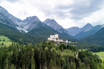 Majestic medieval castle perched on a hillside surrounded by lush forests and towering snow-capped mountains in the Dolomites region