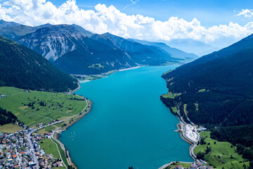 Aerial view of a turquoise lake surrounded by mountains and villages on a sunny day in the alpine region