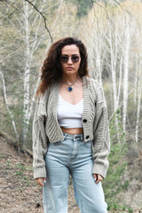 Girl with glasses grey knitted jacket on a forest background