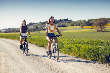 Young women friends cycling while clapping their hands through rapessed field