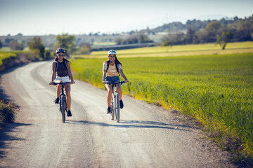 Fototapeta premium Young women friends cycling while clapping their hands through rapessed field