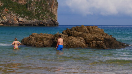 Des gens marchant ou se baignant dans une grande et immense plage bien bondée, avec mer bleu turquois des Astéries, magnifique plage avec ses hauts falaises rayonnant au soleil, temps d'été et période