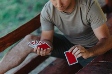 A man skillfully holds a fan of playing cards at an outdoor wooden table, showcasing his concentration and enjoyment in the leisure activity.