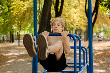 The boy with effort performs a pull-up on the bar with his legs raised in front of him. Athletic...