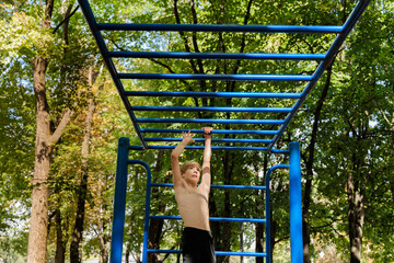 Obraz premium A teenager climbs a horizontal ladder with his hands above his head Athletic teenage boy in the park outdoor workout session