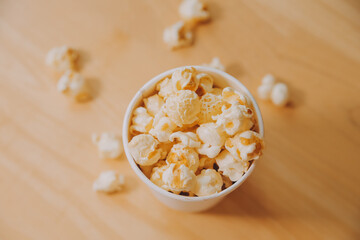 A bucket of popcorn, top-view, warm colors, light brown wooden background, flat lay, daylight macro close-up