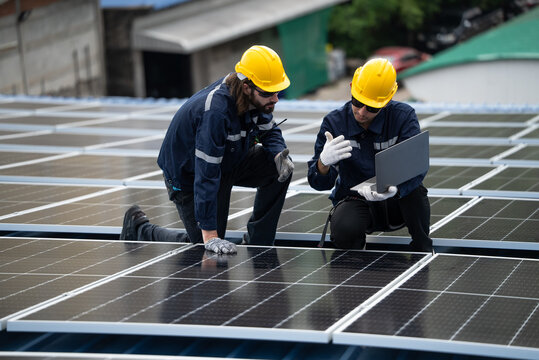 Engineer team checking solar cell  or photovoltaic cell by computer laptop installed on the roof of the factory. Technician worker repair or inspect the system. Industrial renewable energy concept
