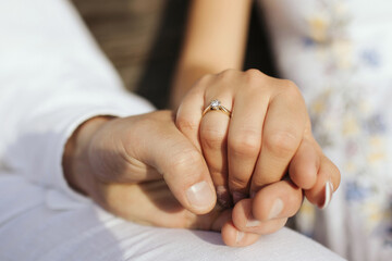 Engagement photo of a couple holding hands. Focus on the engagement ring. Symbol of love and commitment in a romantic sunset light.