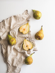 Whole pears and cut pears together with a cloth and a knife over a white counter