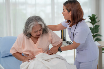 Asian nurse helping a senior Asian female patient with stomach ache on a bed in hospital