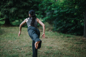 A woman performs a yoga pose in a peaceful forest environment, emphasizing balance, focus, and...