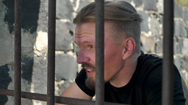 Portrait of a young Caucasian prison inmate in a cage with metal bars. A dangerous repeat offender is caught and arrested. The concept of crime and punishment