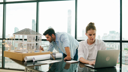 Smart architect engineer inspect house model while colleague using laptop analysis data. Professional designer team working together to design house model construction at modern office. Tracery