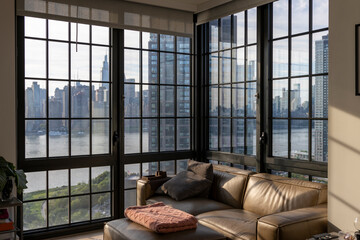 A cozy living room with large windows offering views of the New York City skyline. Highlighting urban architecture and nature