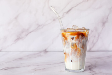 a glass of iced latte coffee with glass straw on white marble table background.