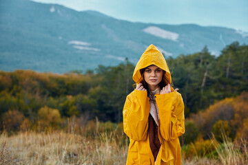Woman in Elegant Yellow Raincoat Enjoying Scenic Mountain View in the Field During Travel Adventure