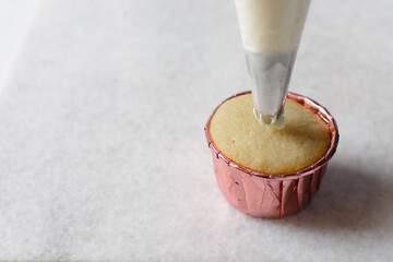 Piping buttercream on a vanilla cupcake, decorating cupcakes, hand piping tall frosting on...