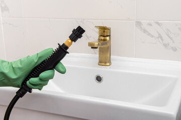 Worker in green gloves cleans the bathroom with steam cleaner. Hot steam and brush cleaning of the sink and faucet. Free space for text