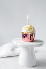 Pink cupcakes with tall buttercream swirl on a cake stand, cupcakes in pink foil liners with vanilla buttercream and a lit candle, frosted cupcakes on a white background