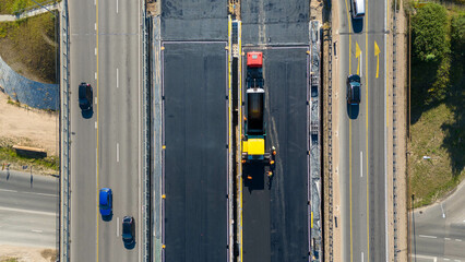 Aerial view of a construction site on a highway, featuring a large asphalt laying machines, and workers